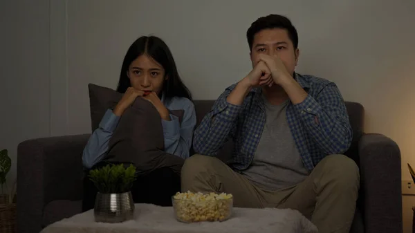 Asian couple in the living room watch a horror movie in the middle of the night.