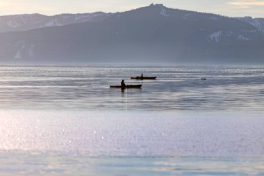 Tahoe Gölü 'nün sisli bir gününde sakin bir yüzeyde kürek çeken iki kanocu.