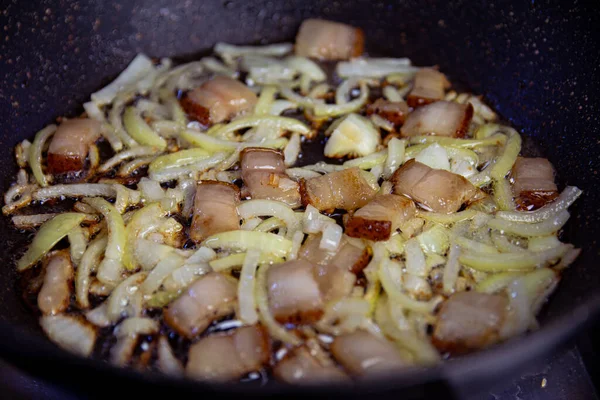 Salo y cebolla finamente picada se fríen en una sartén negra —  Fotos de Stock