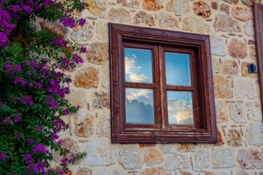 Eski bir kasaba olan Side, Türkiye 'de güzel bir klasik evin penceresi. Bir deniz kabuğu kaya duvarı ve güzel mor çiçekler pencerenin yanındaki duvara tırmanıyor..
