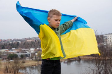 Ukrayna bayrağı taşıyan bir çocuk Ukrayna 'nın bir şehrinde bir gölün ve şehrin arka planına karşı. Ukrayna bayrağıyla vatansever bir çocuğun portresi..