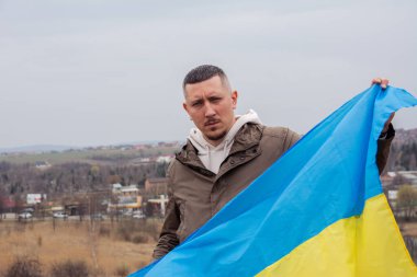 Ukrayna bayrağı taşıyan bir adam Ukrayna 'nın bir şehrinde bir gölün ve şehrin arka planına karşı. Ukrayna bayrağı taşıyan vatansever bir adamın portresi..