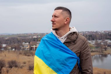 Ukrayna bayrağı taşıyan bir adam Ukrayna 'nın bir şehrinde bir gölün ve şehrin arka planına karşı. Ukrayna bayrağı taşıyan vatansever bir adamın portresi..