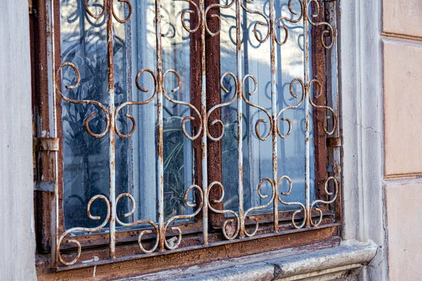 Metal desenli kafesin arkasındaki eski bir evin penceresi. Boya soyan ve paslı parmaklıkları olan eski bir evin arkaplan görüntüsü.