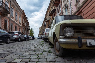 Ukrayna, Chernivtsi, 03.27.2022: Chernivtsi şehrinde park etmiş arabalı sokak. Eski araba Moskvich ön planda. Kenarları kaldırımlı şehir caddesi ve eski binalar..