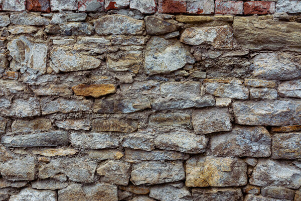 Old stone wall with peeling off plaster. Cracked brickwork, cracked remnants of paint and trim. Texture of vintage brick wall.