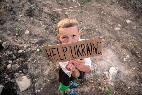 Kirli yüzlü ve üzgün gözlü bir çocuk elinde elinde İngilizce UKRAINE yazısıyla bir karton poster tutuyor. Avrupa görünümlü küçük bir çocuk askeri harekata karşı çıkıyor.