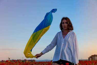 Beyaz gömlekli ve şortlu güzel bir kız gün batımında Ukrayna bayrağıyla haşhaş tarlasında poz veriyor..