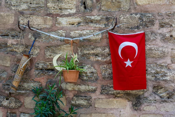 A bow with a quiver and arrows, a Turkish flag and a flower in a pot are hung on a stone wall.