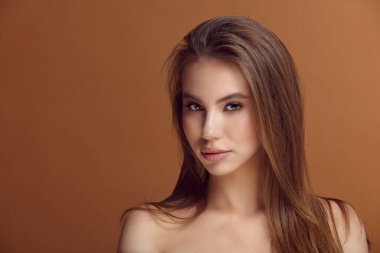 Kahverengi duvarda çıplak omuzları olan baştan çıkarıcı genç bir kadın.