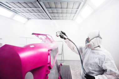 Erkek işçi boya yaptıktan sonra araba gövdesine sprey tabanca sıkar. Otomatik tamir garajı.