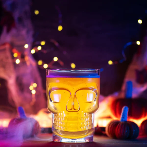 Halloween beer glass skull close-up on a bright glowing background with smoke. Bokeh garland, small pumpkins. Craft beer