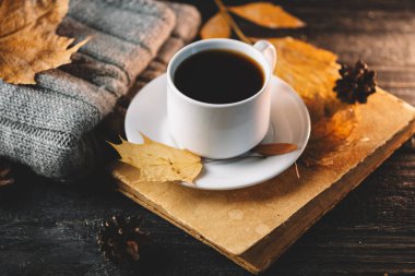 Bir fincan beyaz kahve, sıcak bir örgü süveter, kuru yapraklar ve koniler.