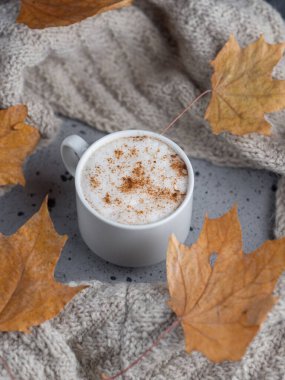 Masanın üzerinde bir kupa tarçınlı latte kahve örgü eşarp ve kuru yapraklarla. Kış zamanı ve rahat ev yapımı sabah kahvaltısı