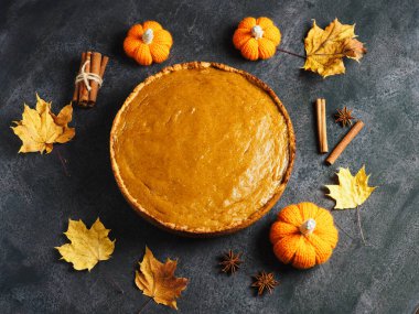 Siyah bir masada geleneksel yuvarlak Amerikan balkabağı turtasının en üst görüntüsü. Balkabakları, tarçın çubukları ve sonbahar akçaağaç yaprakları