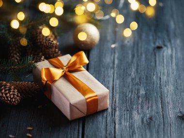 Noel ağacı dalları, koniler ve yan çelenkleri olan ahşap bir masanın üzerinde altın bir kurdele bulunan bir Noel hediyesi kutusu. Boşluğu kopyala