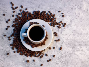 Beyaz espresso fincanının beyaz beton arka planda üst görüntüsü, kavrulmuş kahve çekirdekleri, kopyalama alanı.