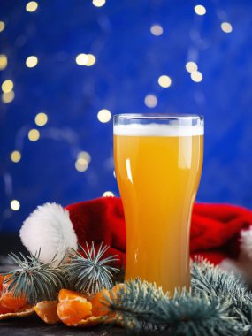 Mavi arka planda mandalinalı bir bardak Noel birası ve Noel Baba şapkalı bir festival masası.