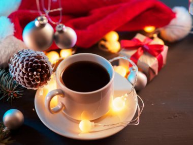 Kutlama masasında beyaz bir fincan espresso, hediyeler, sarı yuvarlak bir çelenk, Noel Baba şapkası ve bir tümsek.
