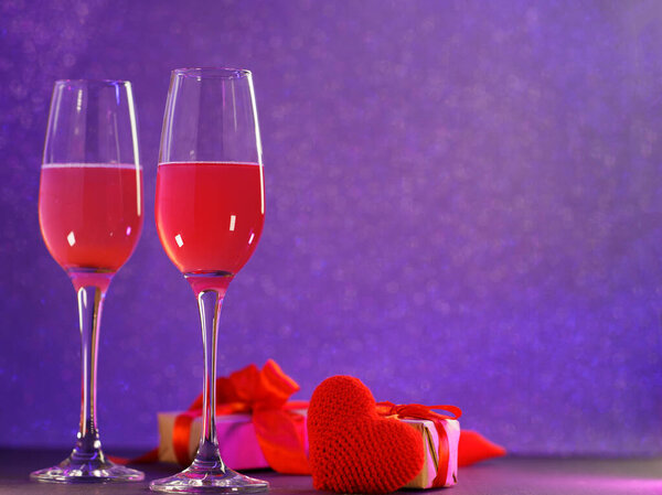 Valentine's day romantic dinner. Two glasses of champagne, gift boxes and a red knitted heart symbol of love. Neon bokeh background and copy space