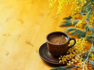 Mimoza çiçekli ahşap bir masanın üzerinde bir fincan kahve.