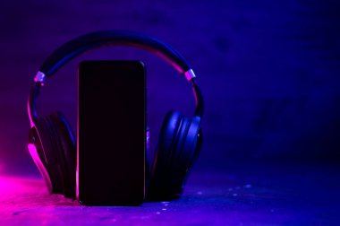 Kulaklık, telefon, müzik dinleme konsepti ya da sesli kitap. Kablosuz kulaklıklı bir akıllı telefon kullan. Neon tarzı fotoğraf.
