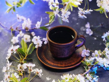 Siyah taştan bir masada, beyaz kirazlı bir dalda sıcak bir fincan kahve. Mavi arkaplan ışığı
