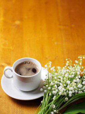 Beyaz bir fincan espresso kahve ve ahşap bir masanın üzerinde bir buket zambak. Bahar geldi.