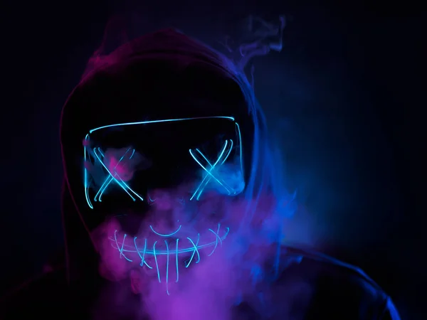 The man hides his face behind a glowing creepy mask. Smoke in the background