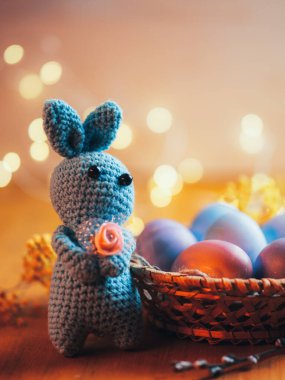 Paskalya tavşanı ve sepet boyalı pastel Paskalya yumurtaları ahşap bir masada, bokeh çelenk