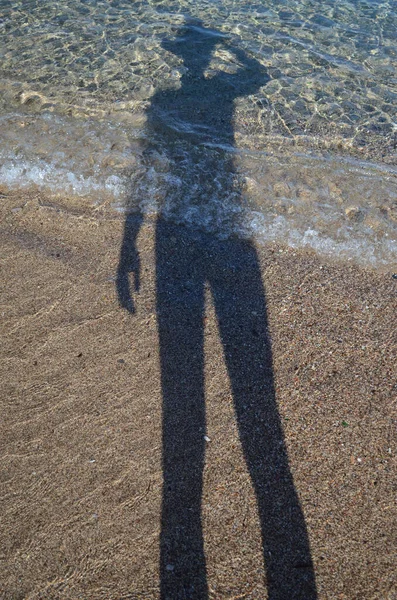 Şapkalı Adam 'ın gölgesi denizin kumları ve sularında