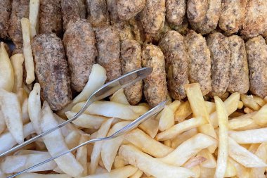 Kadinbudu köftesi ve dilimlenmiş patates. Restoranda çelik maşayla geleneksel Türk yemeği.