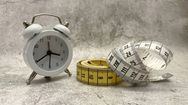 Tape measure and clock on gray floor and background