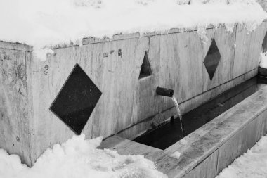 Karda bir çeşme, kışın akan bir çeşme, siyah beyaz fıskiye fotoğrafı.