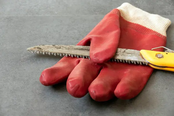 for work safety, it is necessary to work with gloves, there is a hand saw and thick plastic gloves on a floor,