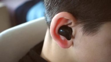 Bir gencin kulağında bluetooth kulaklık var ve müzik dinliyor, kulaklık ve kulaklık takıyor.,