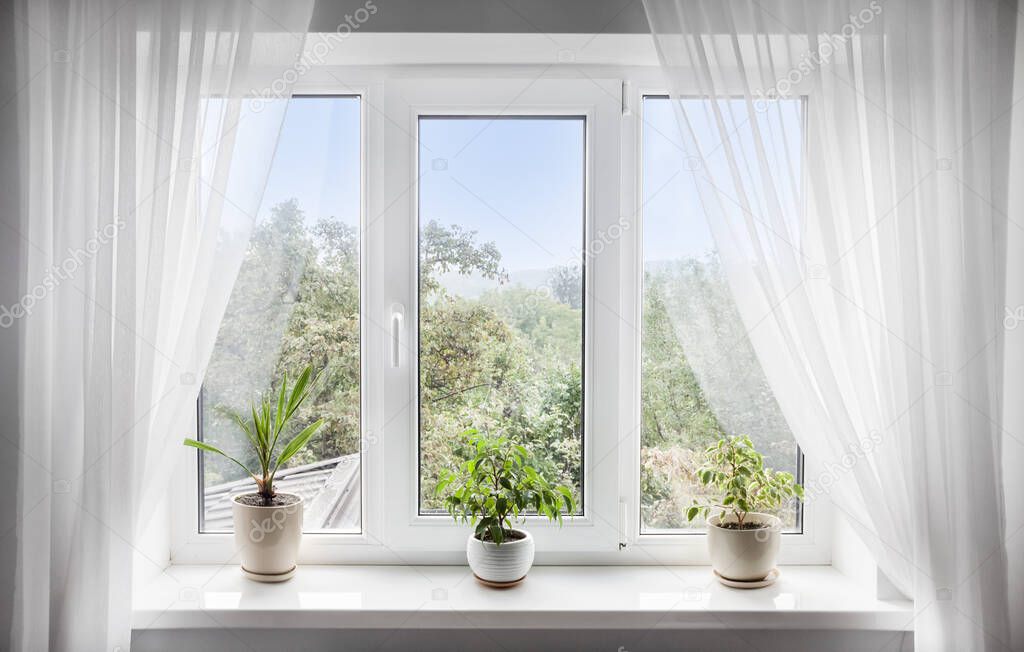 Window with white tulle and potted plants on windowsill. View of nature from the window 