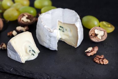 Brie peyniri. Üzümlü yumuşak peynir ve siyah arka planda ceviz.