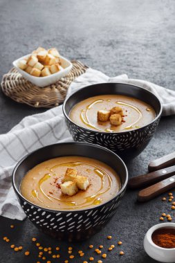 Kırmızı biberli mercimek kremalı çorba ve koyu arkaplanda siyah seramik kaseler. Boşluğu kopyala