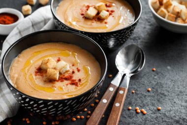 Kırmızı biberli mercimek kremalı çorba ve koyu arkaplanda siyah seramik kaseler. Boşluğu kopyala