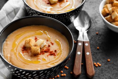 Kırmızı biberli mercimek kremalı çorba ve koyu arkaplanda siyah seramik kaseler.