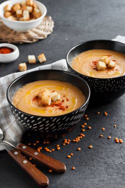 Kırmızı biberli mercimek kremalı çorba ve koyu arkaplanda siyah seramik kaseler.