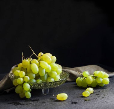 Siyah arka planda cam meyve kasesinde taze yeşil üzümler. Boşluğu kopyala