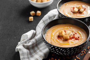 Kırmızı biberli mercimek kremalı çorba ve koyu arkaplanda siyah seramik kaseler. Boşluğu kopyala