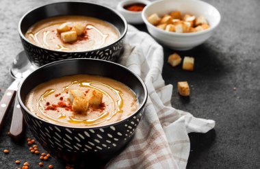 Kırmızı biberli mercimek kremalı çorba ve koyu arkaplanda siyah seramik kaseler.