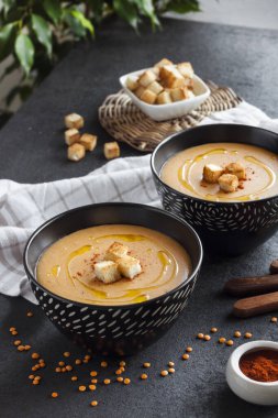 Kırmızı biberli mercimek kremalı çorba ve koyu arkaplanda siyah seramik kaseler.