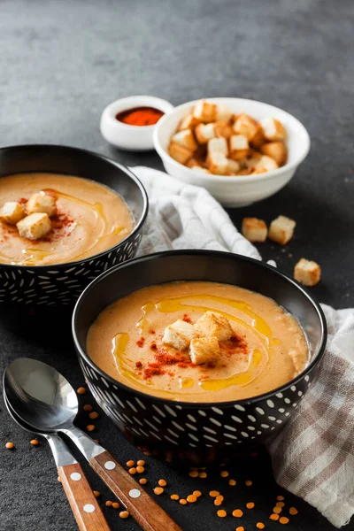 Kırmızı biberli mercimek kremalı çorba ve koyu arkaplanda siyah seramik kaseler.