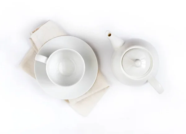 White teapot and empty teacup on pale beige cloth isolated on white background. Flat lay, top view