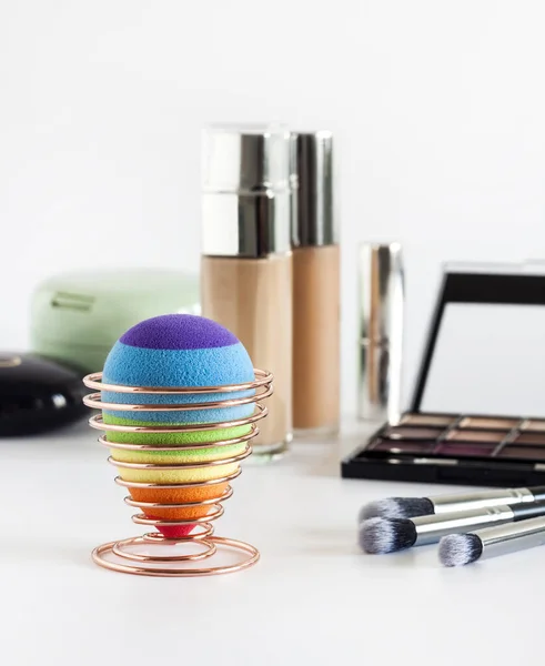 Set of decorative cosmetics on a white background. Rainbow beauty egg sponge on a stand in the foreground