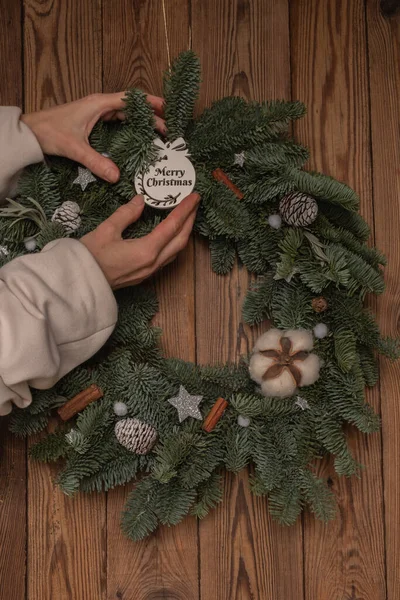 Closeup coniferous holiday wreath on a wooden door. Woman faceless affix inscription Merry Christmas. — 图库照片